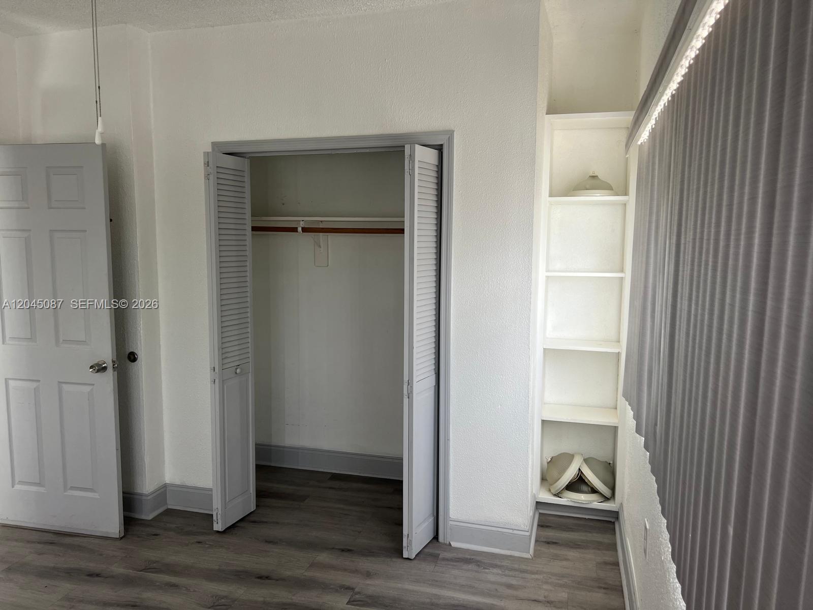 A room features gray wood-look flooring, a closet with louvered doors, and built-in white shelving — 1322 SW 7th St # 8, Miami FL 33135, MIAMI, FL