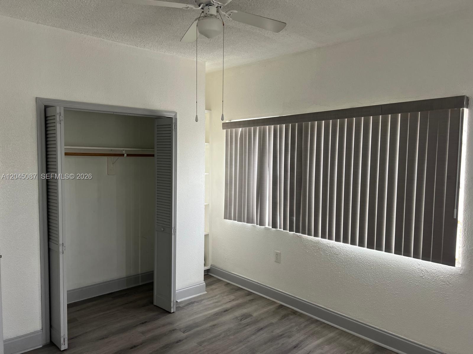 This bedroom features gray wood-look flooring, a closet with louvered doors, and vertical window blinds — 1322 SW 7th St # 8, Miami FL 33135, MIAMI, FL