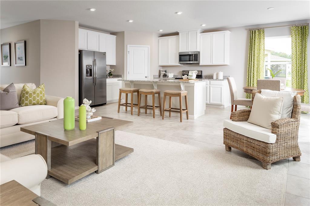 An open-concept kitchen and living area features white cabinetry, stainless appliances, and neutral furniture — 1739 UPLAND LANE, WINTER HAVEN, FL