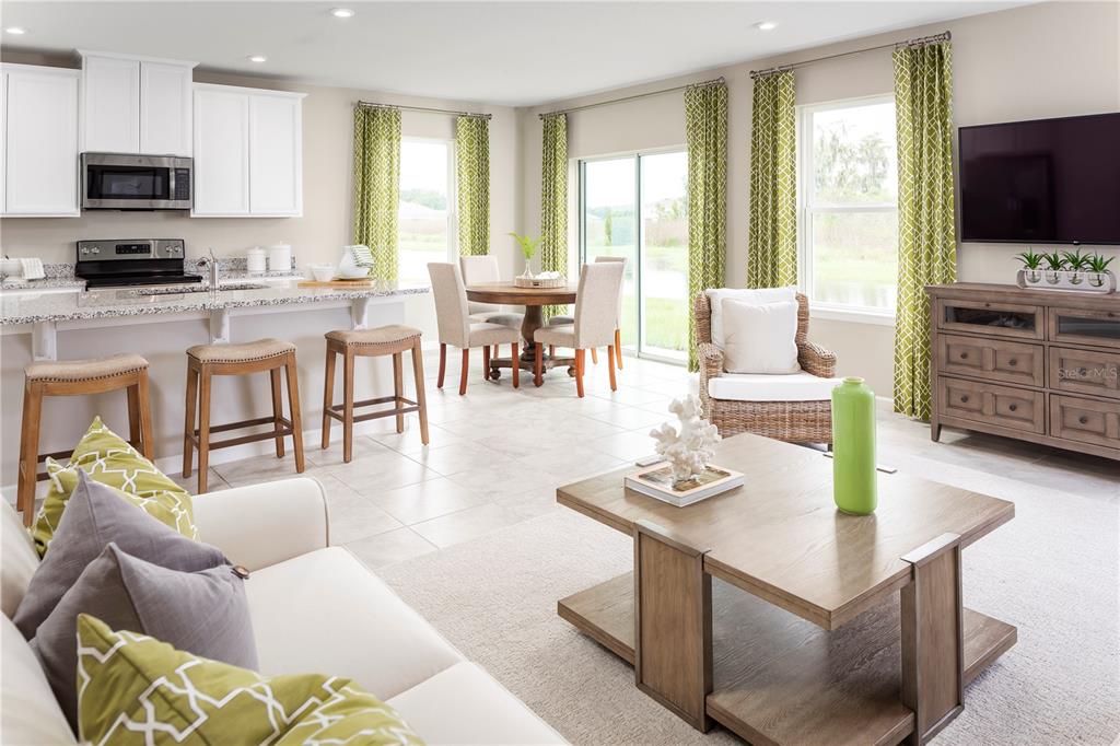An open-concept kitchen, dining area, and living room with tile floors and green patterned curtains — 1739 UPLAND LANE, WINTER HAVEN, FL