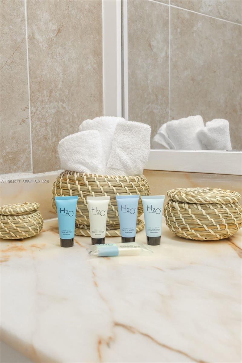 A marble bathroom vanity displays a basket of white towels and H2O toiletries — 5445 Collins Ave # 1623, Miami Beach FL 33140, MIAMI BEACH, FL