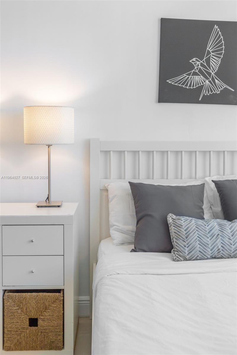 A bedroom features a white bed frame, a white nightstand with a lamp, and wall art — 5445 Collins Ave # 1623, Miami Beach FL 33140, MIAMI BEACH, FL