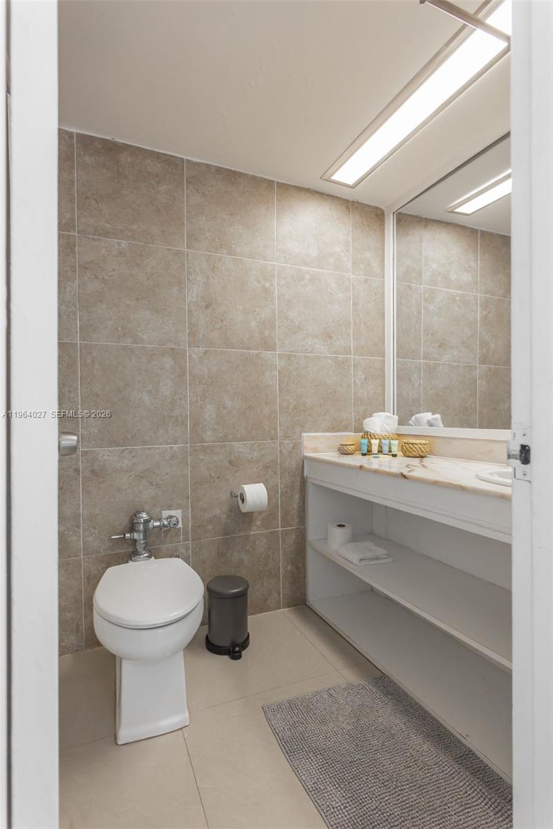 A bathroom features beige tiled walls, a white toilet, and an open-shelf vanity — 5445 Collins Ave # 1623, Miami Beach FL 33140, MIAMI BEACH, FL