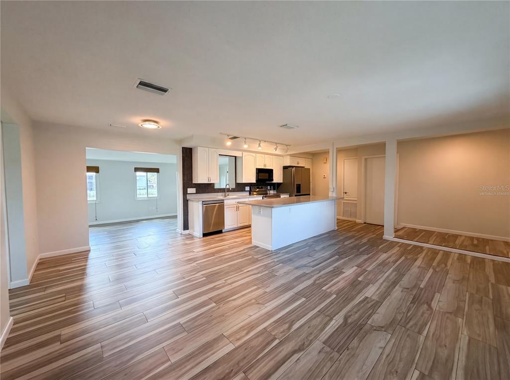 An open-concept kitchen features white cabinetry, a central island, and wood-look flooring — 3260 PINETREE STREET, PORT CHARLOTTE, FL