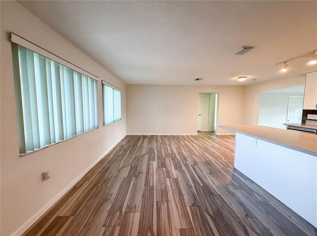 An open-concept living area features wood-look tile flooring, vertical blinds, and a kitchen peninsula — 3260 PINETREE STREET, PORT CHARLOTTE, FL