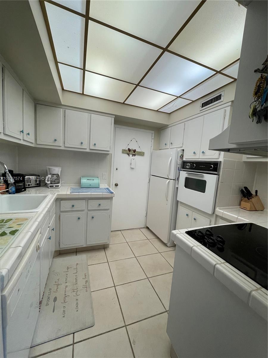 A kitchen features white cabinets, tile countertops, a drop ceiling, and white appliances — 3505 S Ocean Dr # 921, Hollywood FL 33019, HOLLYWOOD, FL