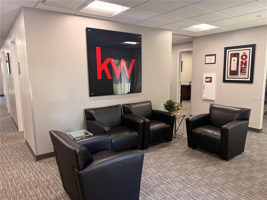 A waiting area features four black leather armchairs, a KW logo sign, and gray carpeting — 30522 US HIGHWAY 19 N UNIT 105, PALM HARBOR, FL