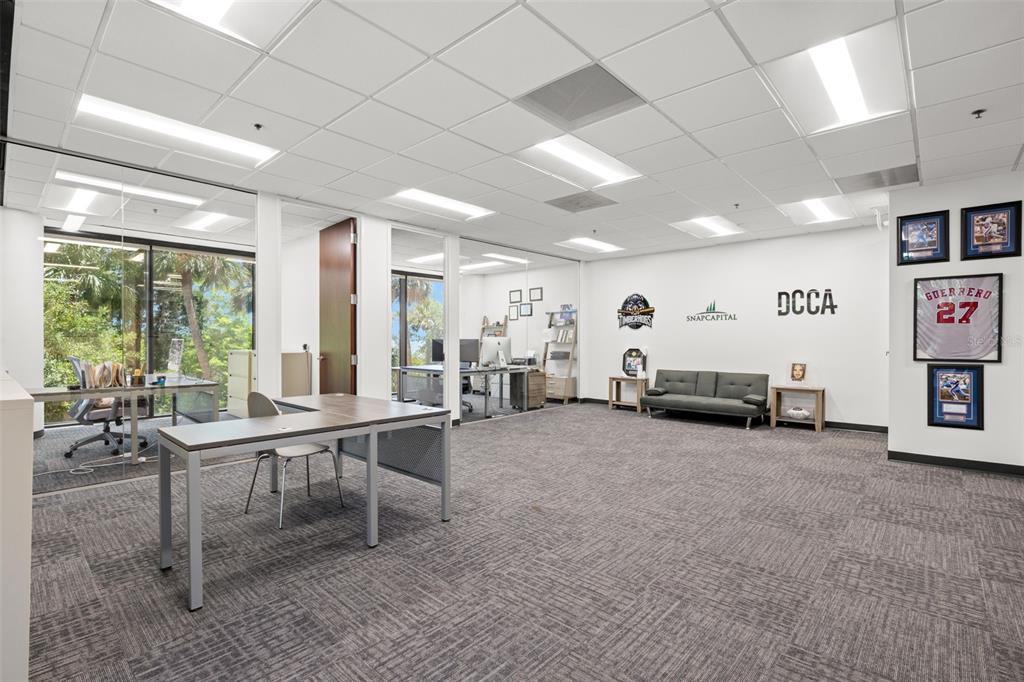 An office space features gray carpet, drop ceilings, glass-walled partitions, and framed sports memorabilia — 2701 N ROCKY POINT DRIVE UNIT 105, TAMPA, FL