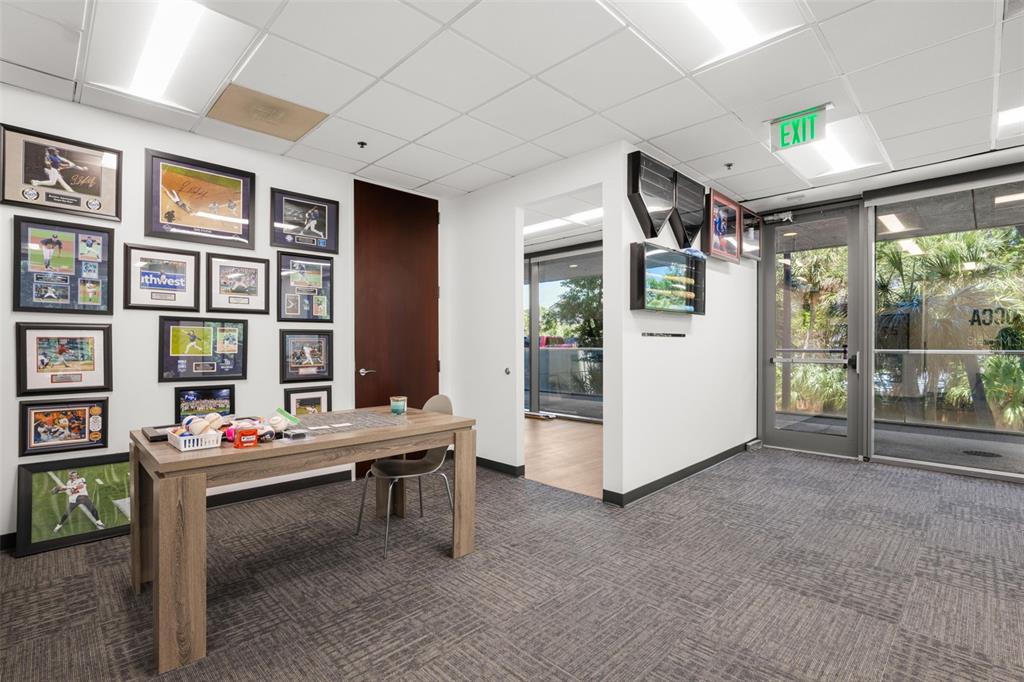 An office space features a wooden desk, sports memorabilia on the walls, and glass doors — 2701 N ROCKY POINT DRIVE UNIT 105, TAMPA, FL