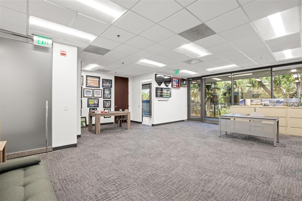 An office space features a gray carpet, drop ceiling, two desks, and a glass wall — 2701 N ROCKY POINT DRIVE UNIT 105, TAMPA, FL