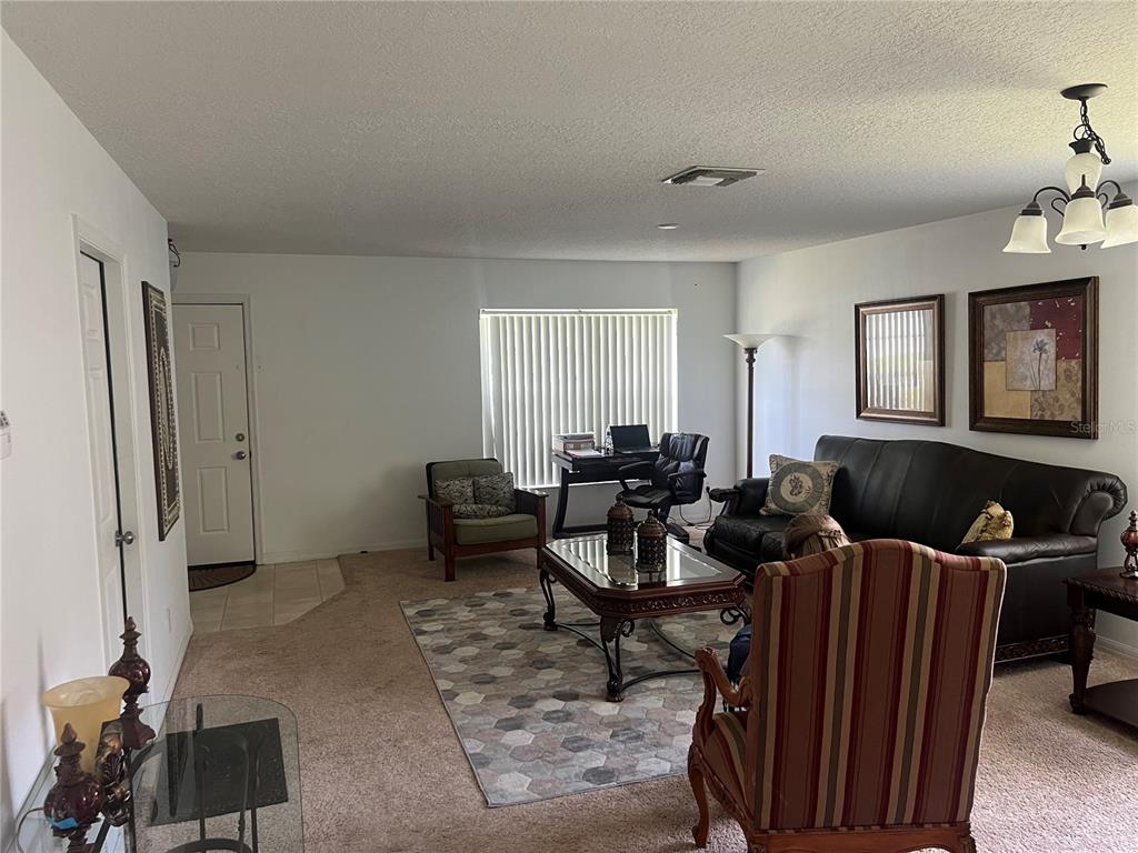 A living room features a dark leather sofa, a striped armchair, and a home office area — 1815 AMERICUS MINOR DRIVE, WINTER GARDEN, FL