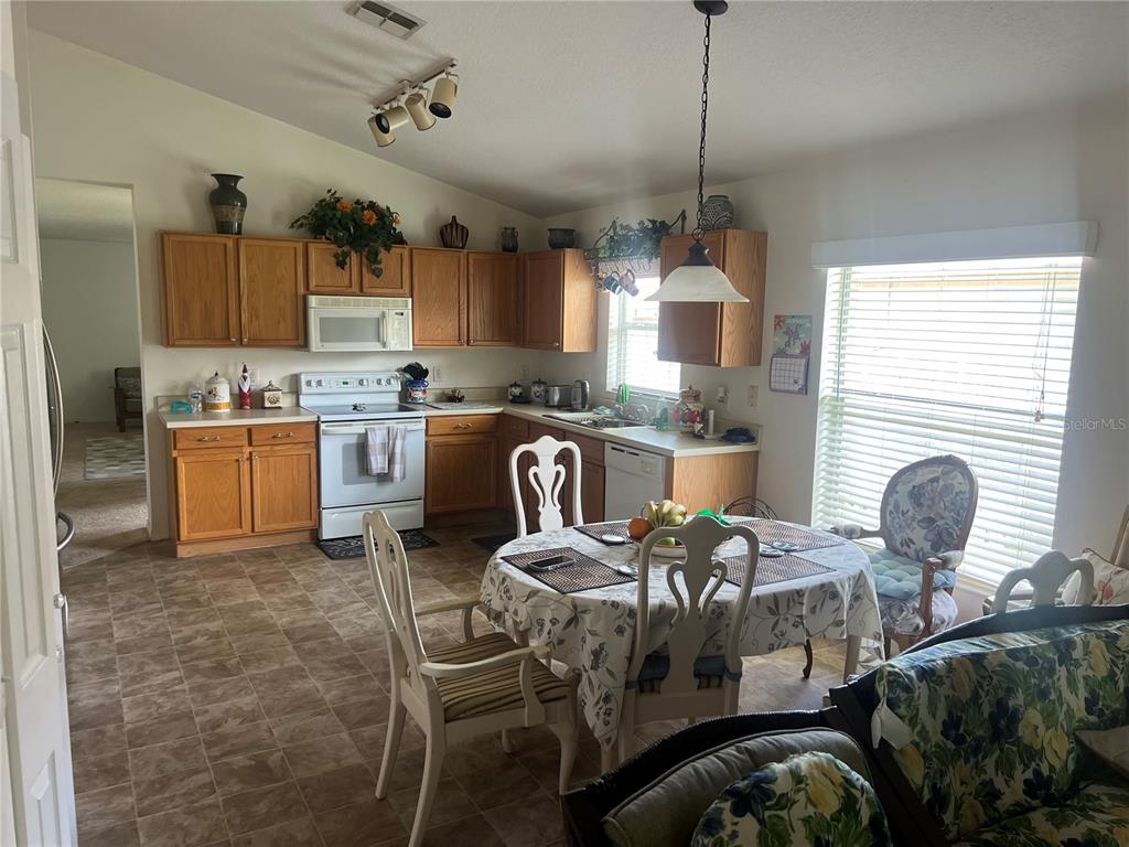 A kitchen features wood cabinets, white appliances, a dining table, and tile flooring — 1815 AMERICUS MINOR DRIVE, WINTER GARDEN, FL