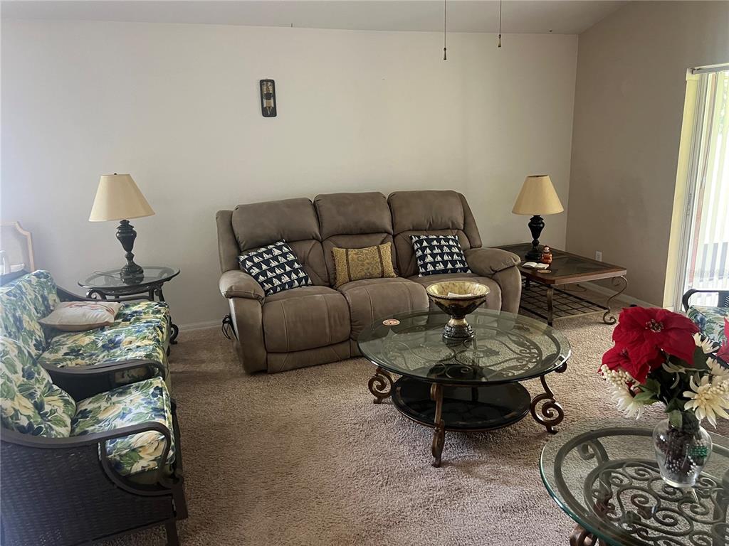 A living room features a brown reclining sofa, floral chairs, and glass-topped tables on carpet — 1815 AMERICUS MINOR DRIVE, WINTER GARDEN, FL
