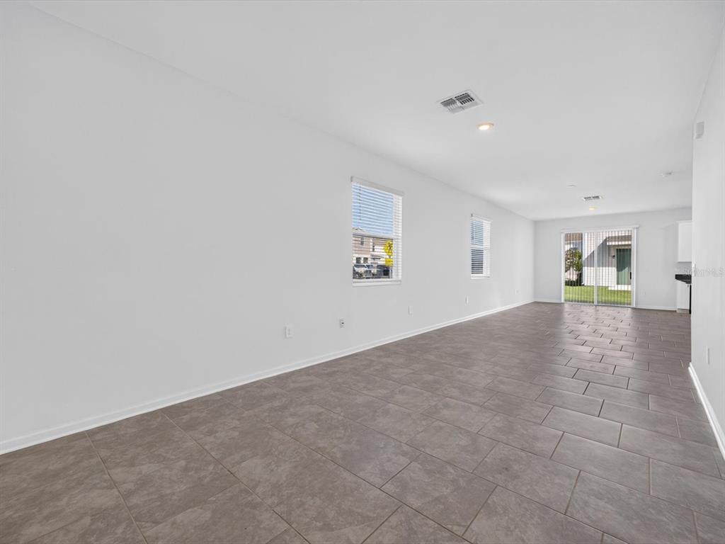 An empty room with white walls, gray tile flooring, two windows, and sliding glass doors — 2413 BROOK MARSH LOOP, KISSIMMEE, FL