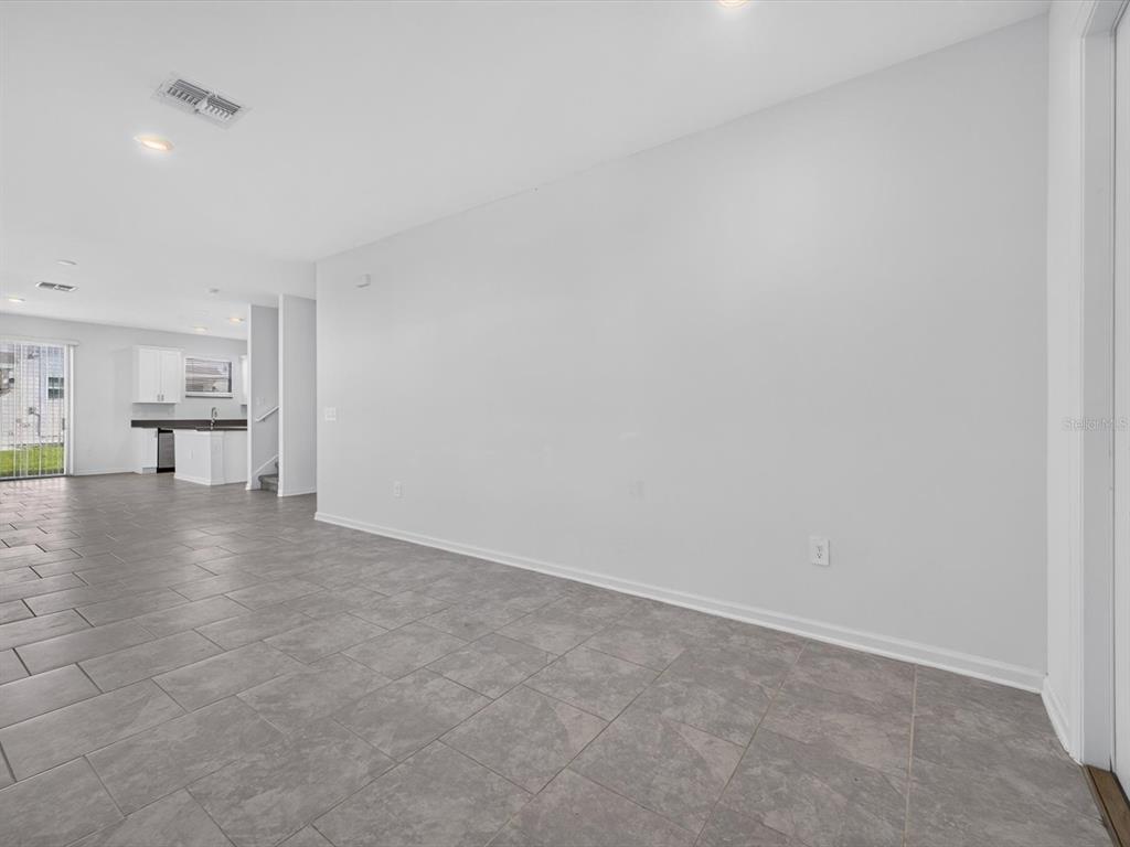 A spacious room with light gray walls, tile flooring, and a view into the kitchen — 2413 BROOK MARSH LOOP, KISSIMMEE, FL