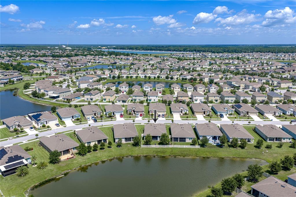 An aerial view shows a suburban neighborhood with houses surrounding a central pond — 31785 TANSY BEND, WESLEY CHAPEL, FL