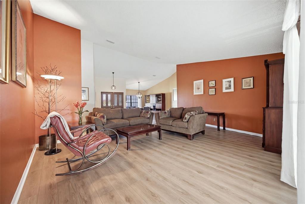 A living room with orange walls, brown sofas, a rocking chair, and light wood flooring — 13707 ATTLEY PLACE, TAMPA, FL