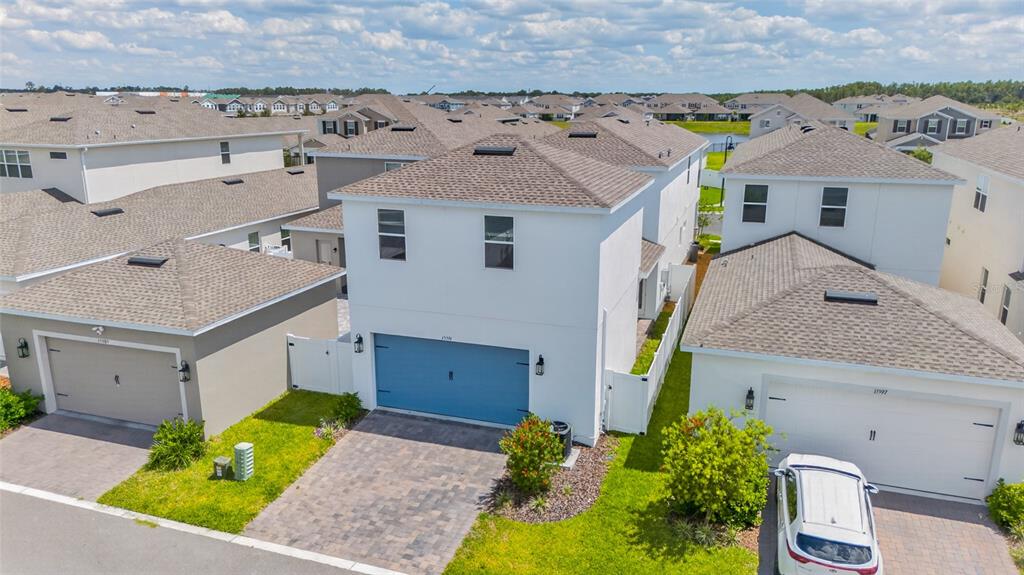 An aerial view shows three suburban houses with paved driveways and attached garages — 15591 GENTLE RAIN DRIVE, WINTER GARDEN, FL