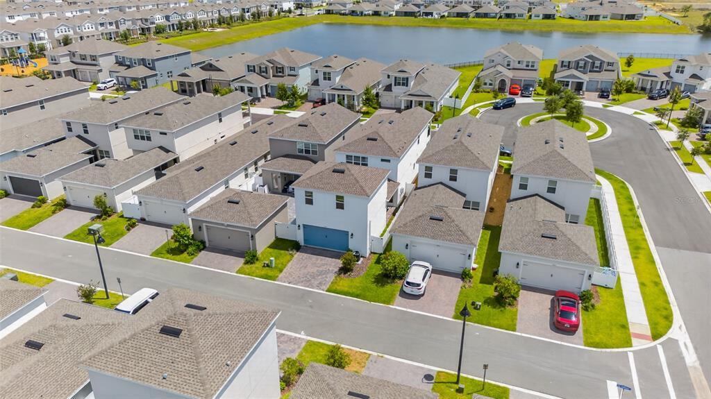 An aerial view shows a suburban neighborhood with multiple houses, driveways, and a nearby pond — 15591 GENTLE RAIN DRIVE, WINTER GARDEN, FL