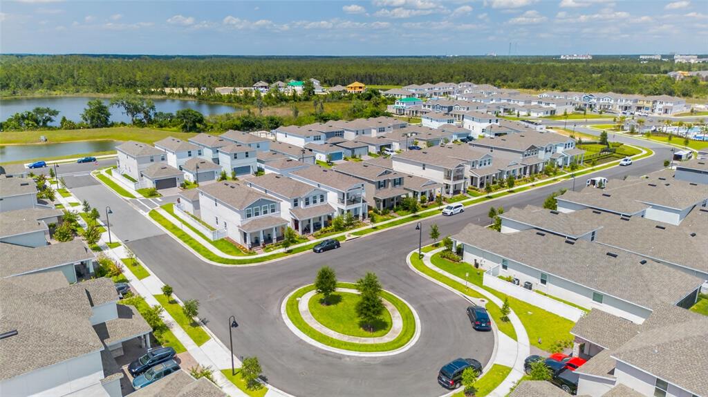 An aerial view shows a suburban neighborhood with houses, a roundabout, and a nearby lake — 15591 GENTLE RAIN DRIVE, WINTER GARDEN, FL