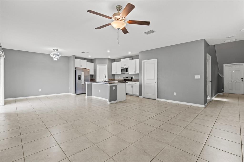 An open-concept kitchen and living area with light tile flooring, grey walls, and white cabinetry — 16671 KINGMAN REEF STREET, WIMAUMA, FL