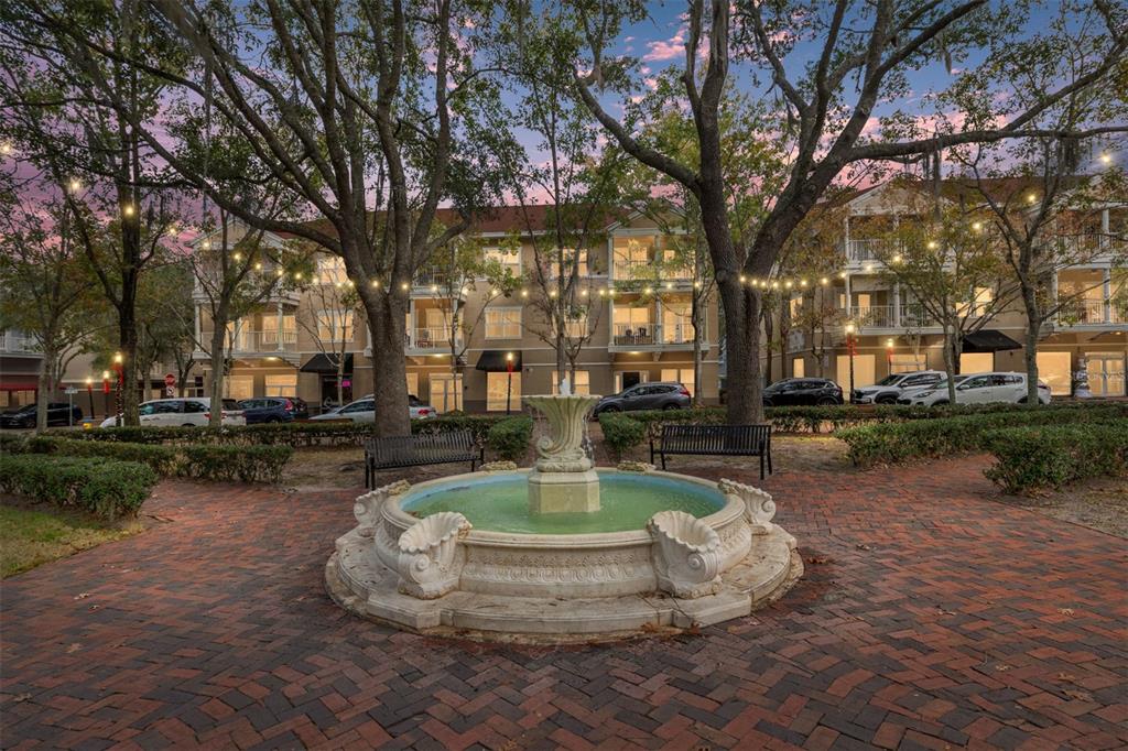 A stone fountain sits in the center of a brick plaza surrounded by trees and buildings — 5015 SW 91 TERRACE, GAINESVILLE, FL