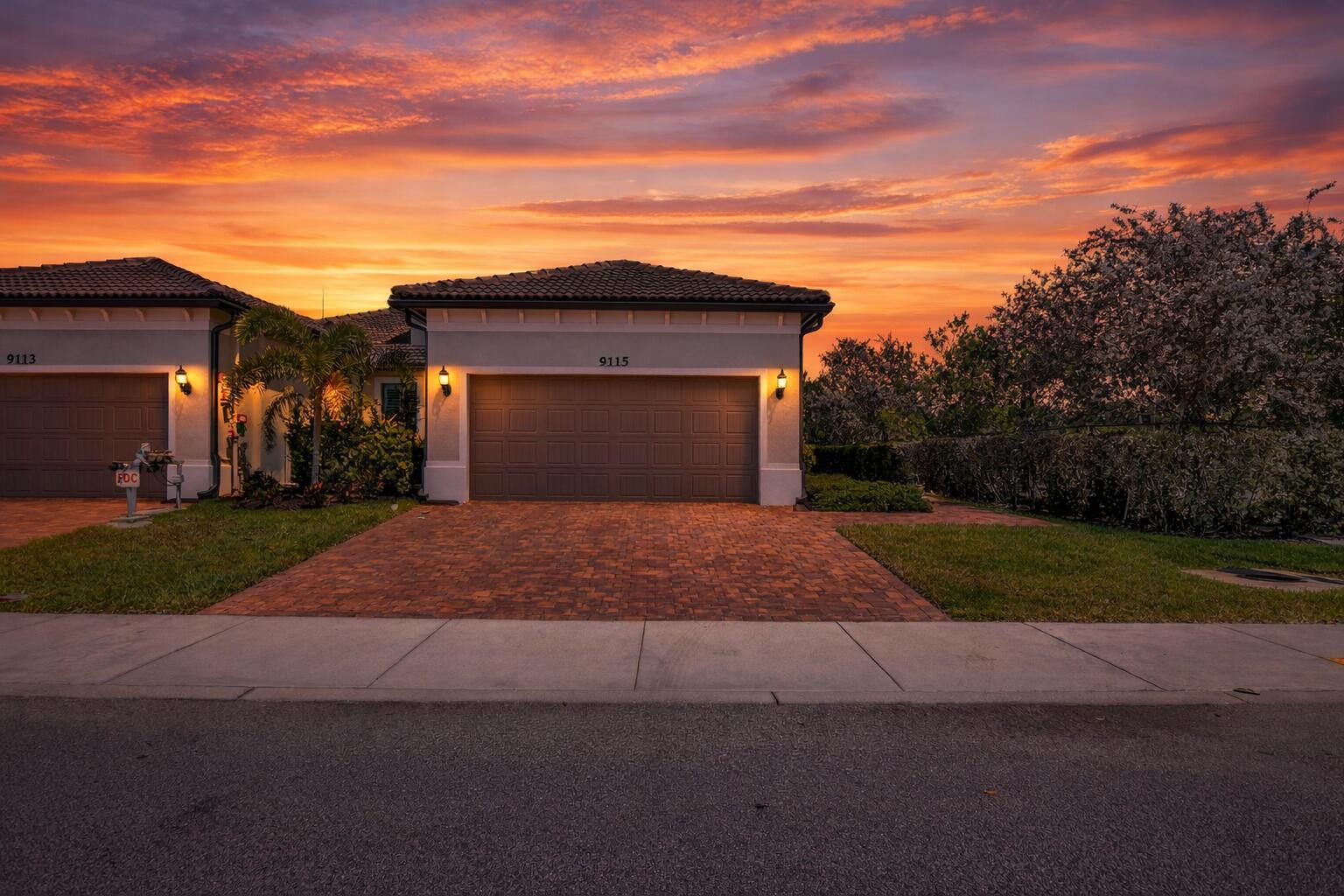 A suburban house exterior with a two-car garage and a brick driveway at sunset — 9115 Passiflora Way, Boca Raton FL 33428, BOCA RATON, FL