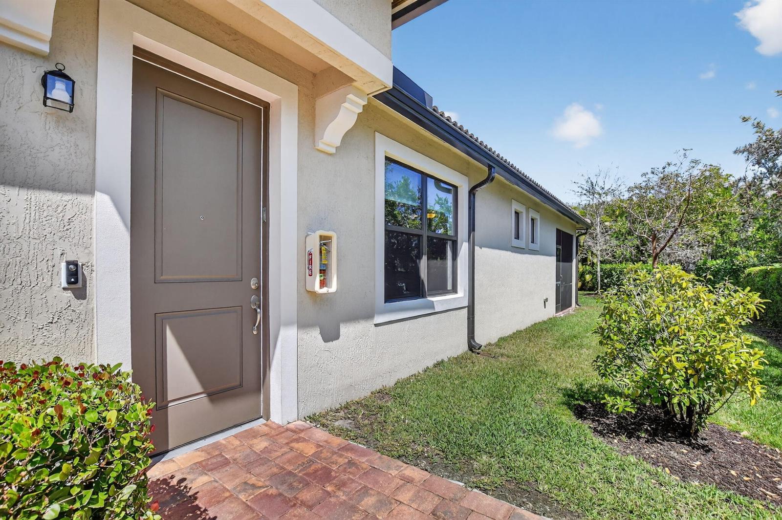 A tan house exterior features a brown front door, a window, and a fire extinguisher — 9115 Passiflora Way, Boca Raton FL 33428, BOCA RATON, FL
