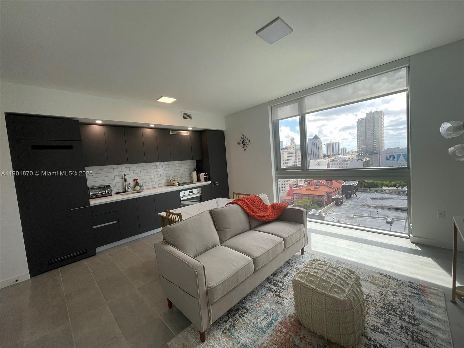 A modern studio apartment features a dark kitchen, a sofa, and floor-to-ceiling city views — 227 NE 2nd St # 1606, Miami FL 33132, MIAMI, FL