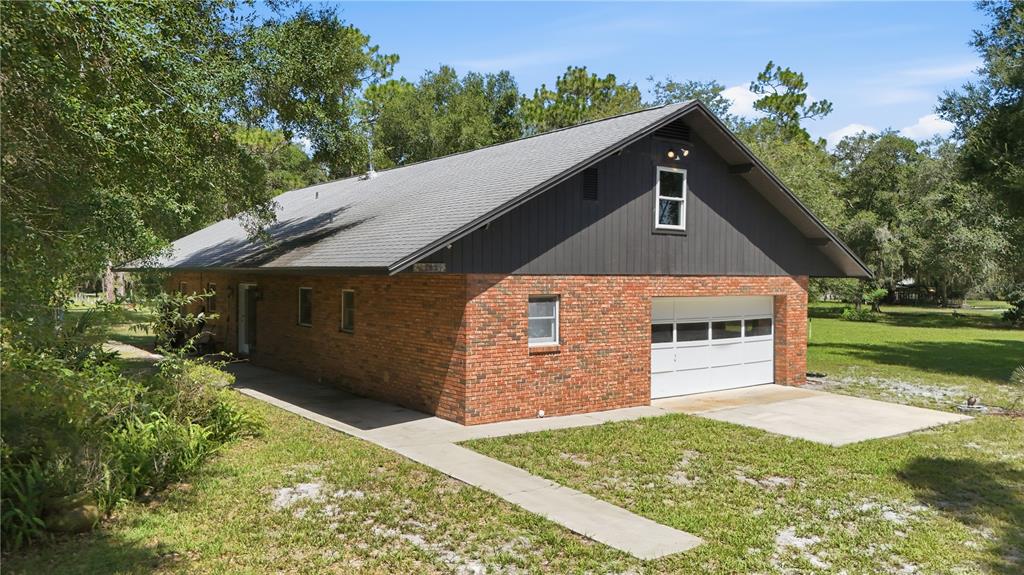 A brick house with a white garage door, dark siding, and a gray shingled roof — 163 E ORANGE AVENUE, PIERSON, FL