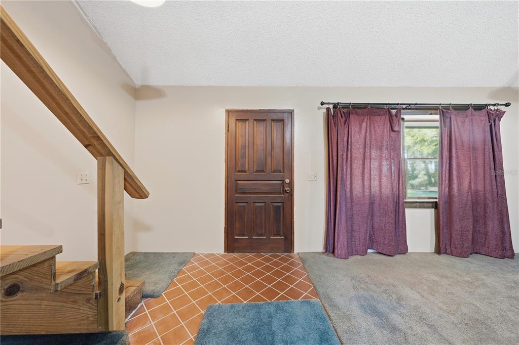 An interior view shows a wooden staircase, a tiled entryway, and a carpeted living area — 163 E ORANGE AVENUE, PIERSON, FL