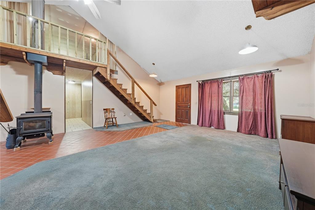 A living room features a wood-burning stove, a staircase to a loft, and carpeted flooring — 163 E ORANGE AVENUE, PIERSON, FL