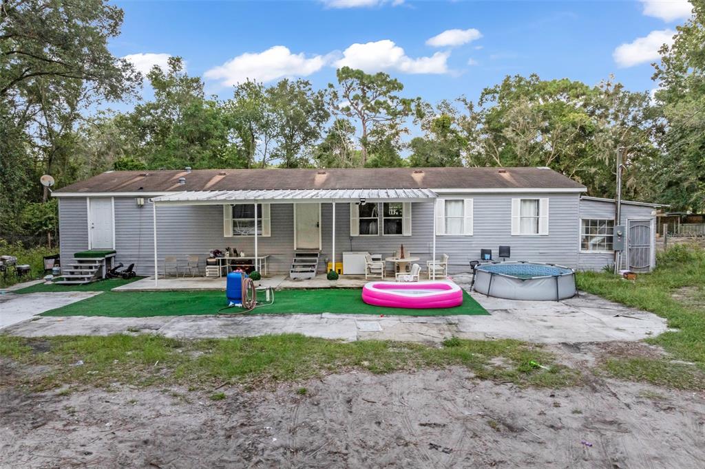 The exterior of a single-story gray house features a metal patio cover and above-ground pool — 15816 NORTHGATE LANE, SPRING HILL, FL
