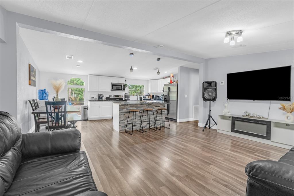 An open-concept living room and kitchen featuring wood-look flooring, white cabinetry, and a stone island — 15816 NORTHGATE LANE, SPRING HILL, FL