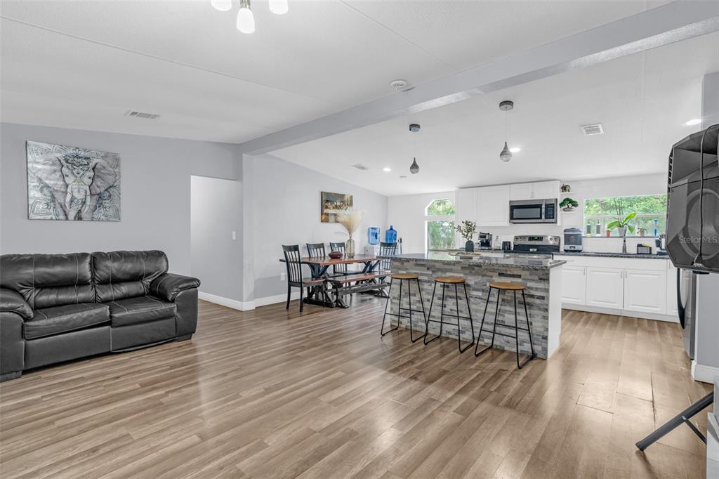 An open-concept living room and kitchen featuring wood-look flooring, a stone-faced island, and white cabinetry — 15816 NORTHGATE LANE, SPRING HILL, FL