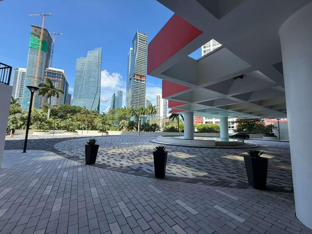 A paved outdoor plaza features modern planters and a covered entrance beneath tall city skyscrapers — 1581 Brickell Avenue # 406, Miami FL 33129, MIAMI, FL
