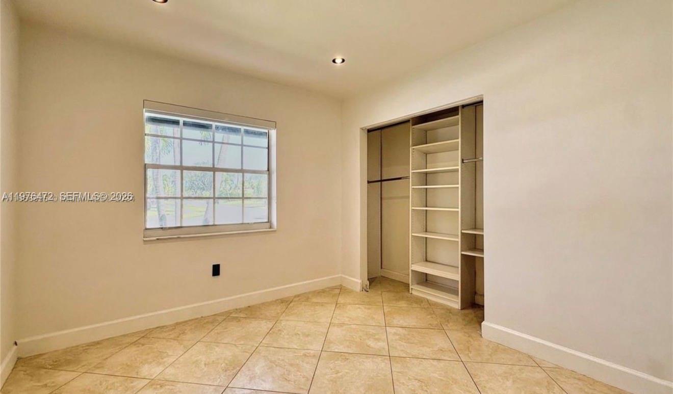 A bedroom features beige tile flooring, a window with grid panes, and a built-in closet — 21020 NE 18th Ct, Miami FL 33179, MIAMI, FL