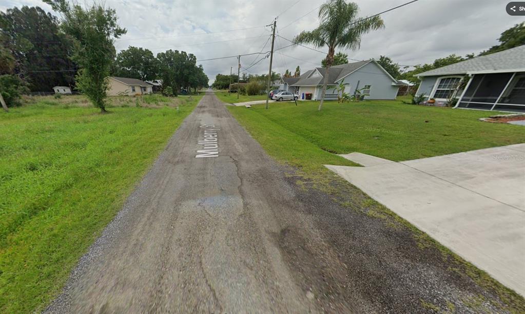 A narrow, paved residential street with houses on the right and an empty lot left — 8435 PATTERSON AVENUE, SEBASTIAN, FL