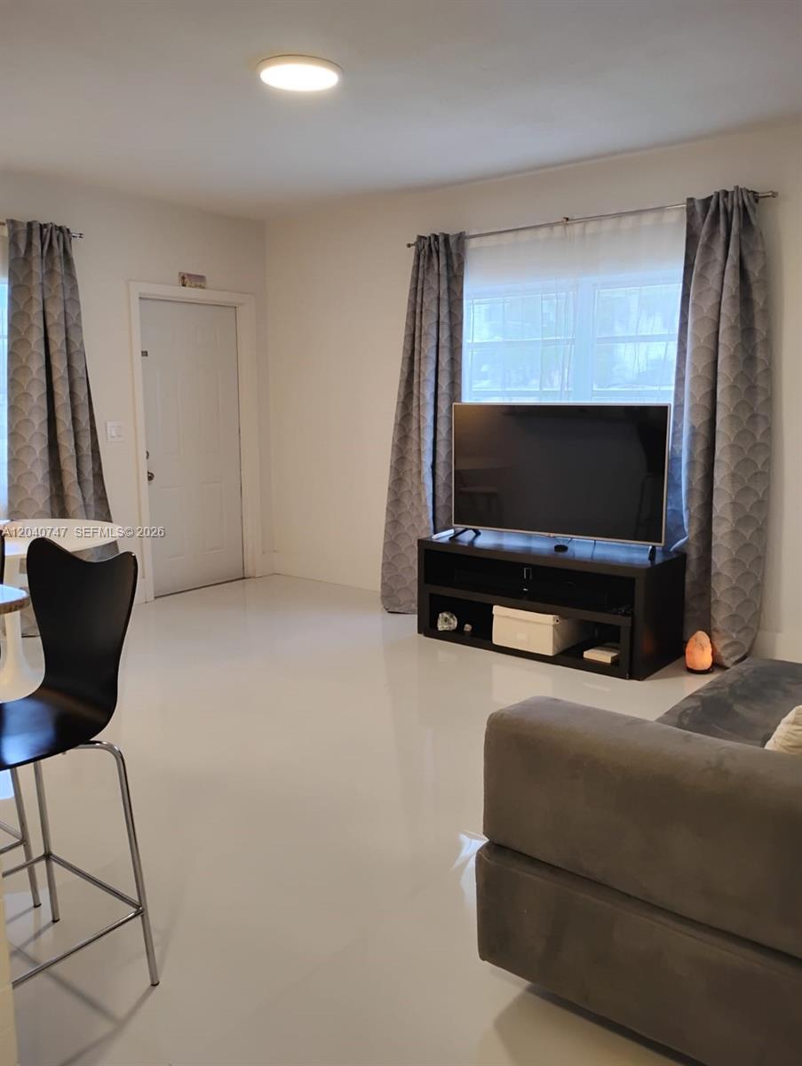 A living room features white tile flooring, a television on a stand, and gray curtains — HOLLYWOOD, FL