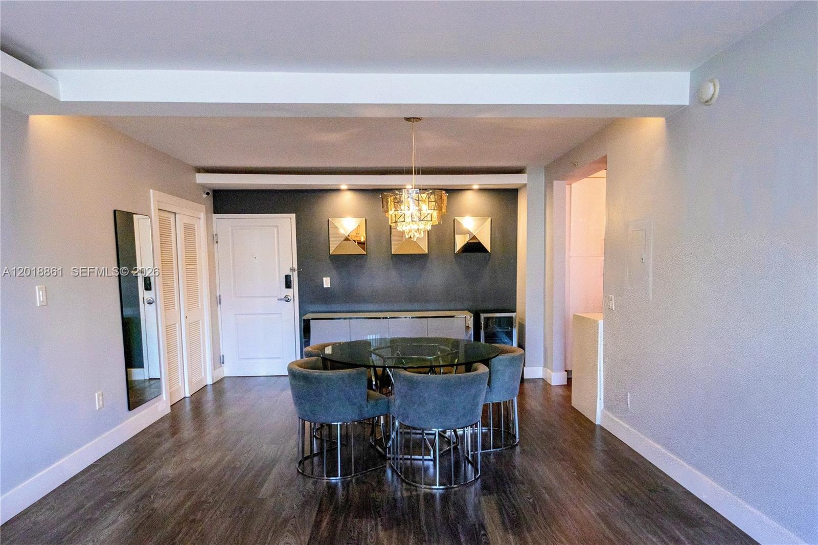 A dining room features a glass-topped table, grey upholstered chairs, and a dark accent wall — 401 69th St # 212, Miami Beach FL 33141, MIAMI BEACH, FL