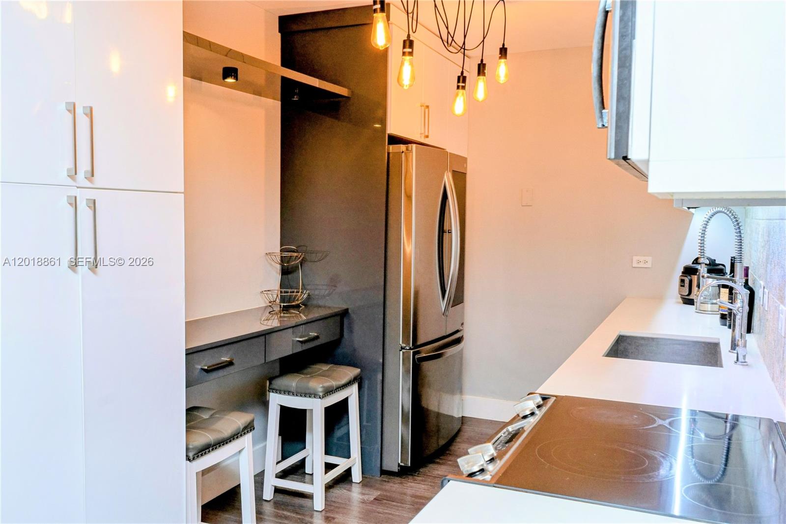 A modern kitchen features white cabinetry, stainless steel appliances, and a small built-in desk area — 401 69th St # 212, Miami Beach FL 33141, MIAMI BEACH, FL