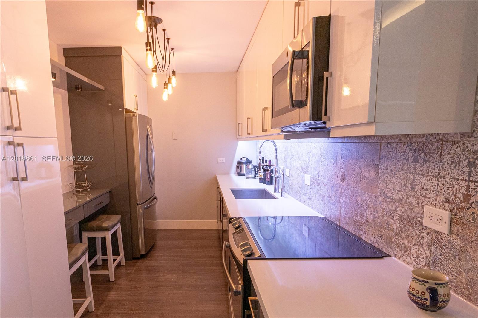 A modern galley kitchen features white cabinetry, stainless steel appliances, and patterned tile backsplashes — 401 69th St # 212, Miami Beach FL 33141, MIAMI BEACH, FL