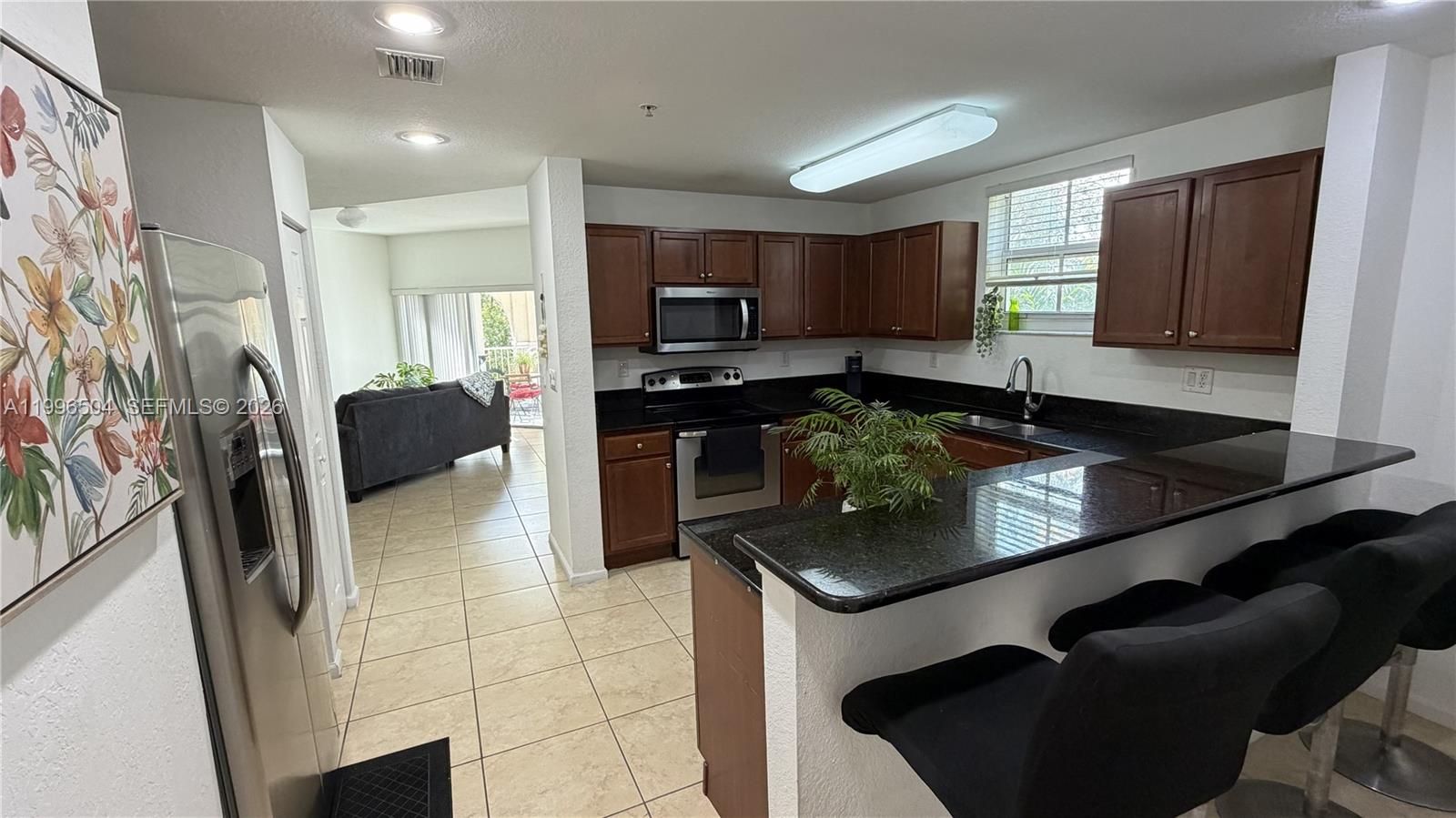 A kitchen features dark wood cabinets, black granite countertops, stainless steel appliances, and tile flooring — 11605 NW 89th St # 220, Doral FL 33178, DORAL, FL