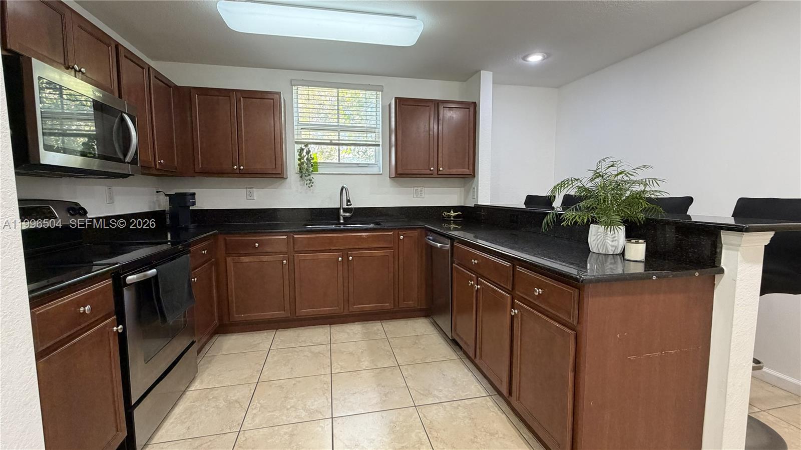 A kitchen features dark wood cabinets, black countertops, stainless steel appliances, and tile flooring — 11605 NW 89th St # 220, Doral FL 33178, DORAL, FL