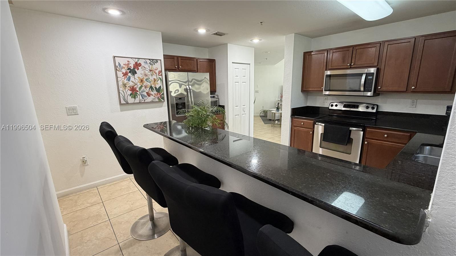 A kitchen features dark wood cabinets, black granite countertops, stainless steel appliances, and bar seating — 11605 NW 89th St # 220, Doral FL 33178, DORAL, FL