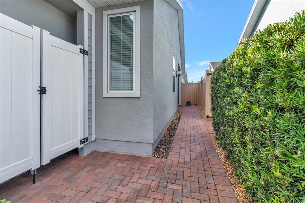 A brick walkway leads along the side of a house past a white privacy fence — 78 BAYOU BEND ROAD, GROVELAND, FL