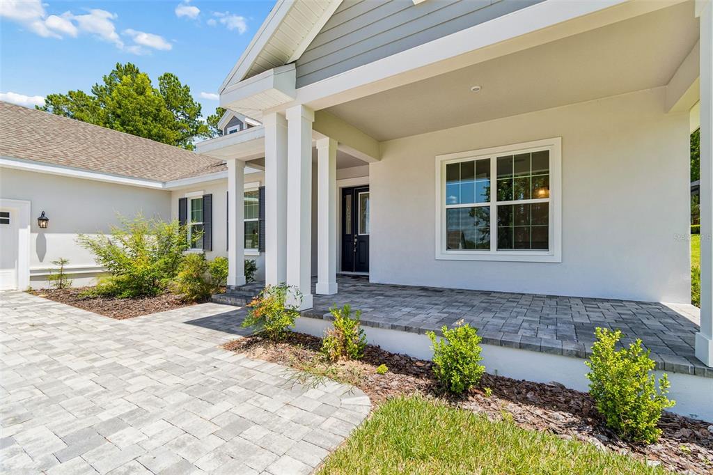 A paved walkway leads to the covered front porch of a white house with columns — 4880 HICKORY OAK DRIVE, BROOKSVILLE, FL