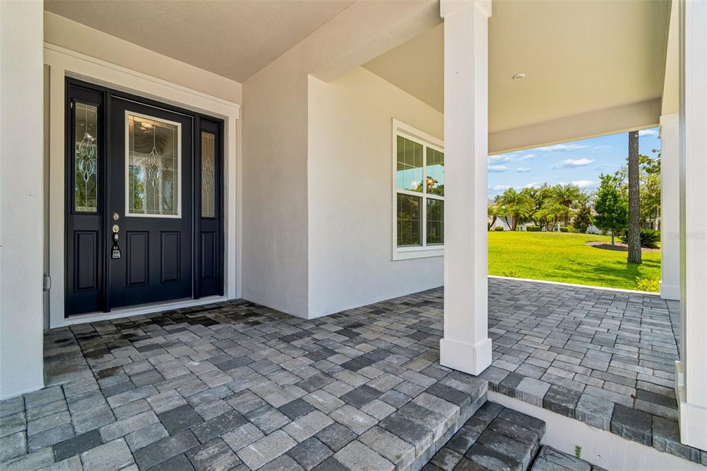 A covered front porch with paver flooring leads to a dark blue front door — 4880 HICKORY OAK DRIVE, BROOKSVILLE, FL
