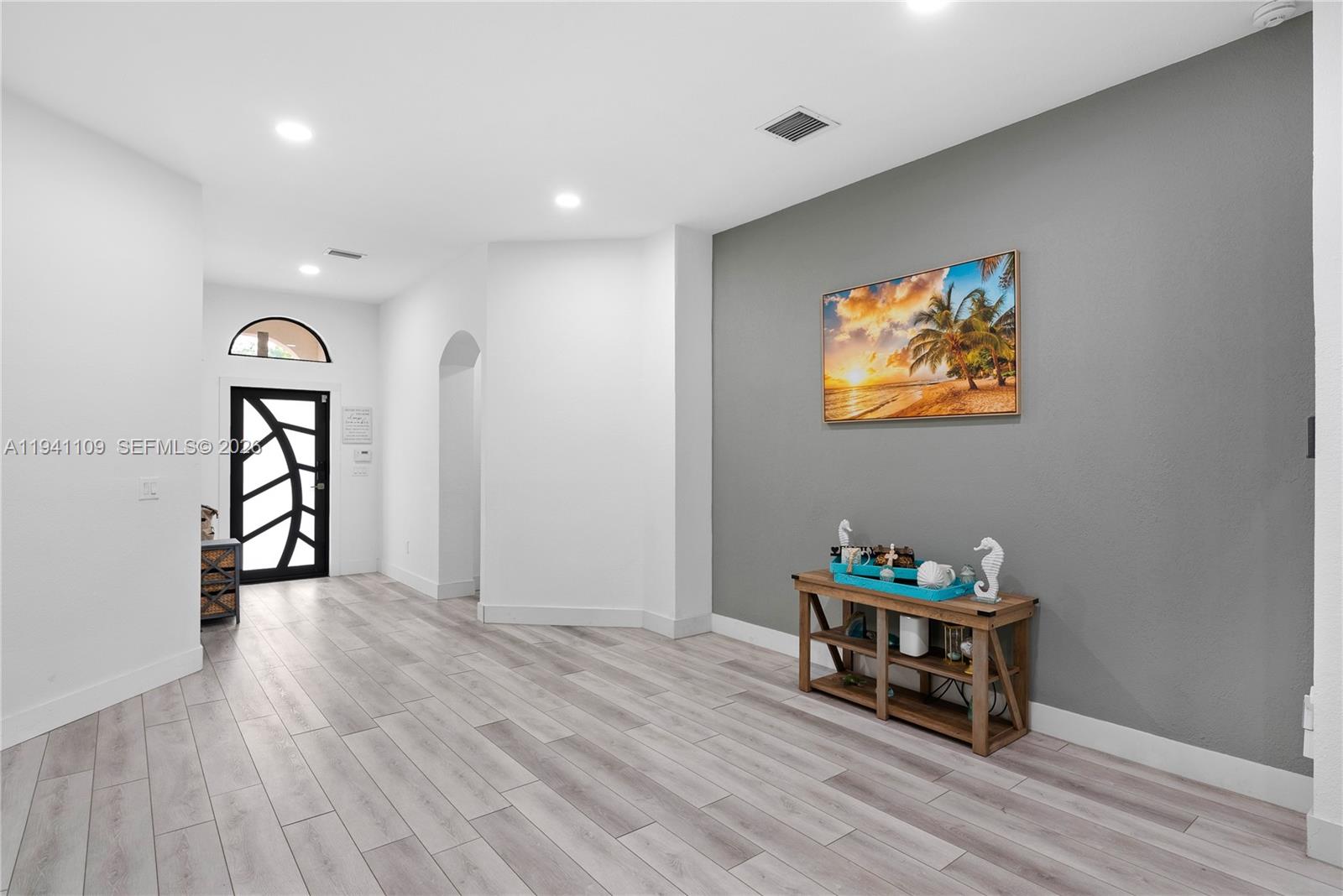 An entryway features light wood-look flooring, a gray accent wall with artwork, and a console table — 918 NE 36th Ave, Homestead FL 33033, HOMESTEAD, FL