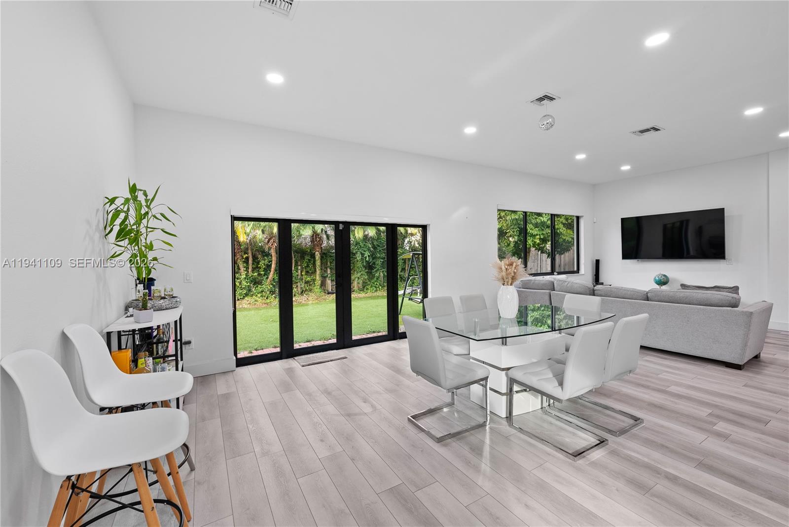 A bright, open-concept dining and living area features white walls, light wood flooring, and glass doors — 918 NE 36th Ave, Homestead FL 33033, HOMESTEAD, FL